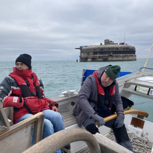 Two men on boat with old fort behind them